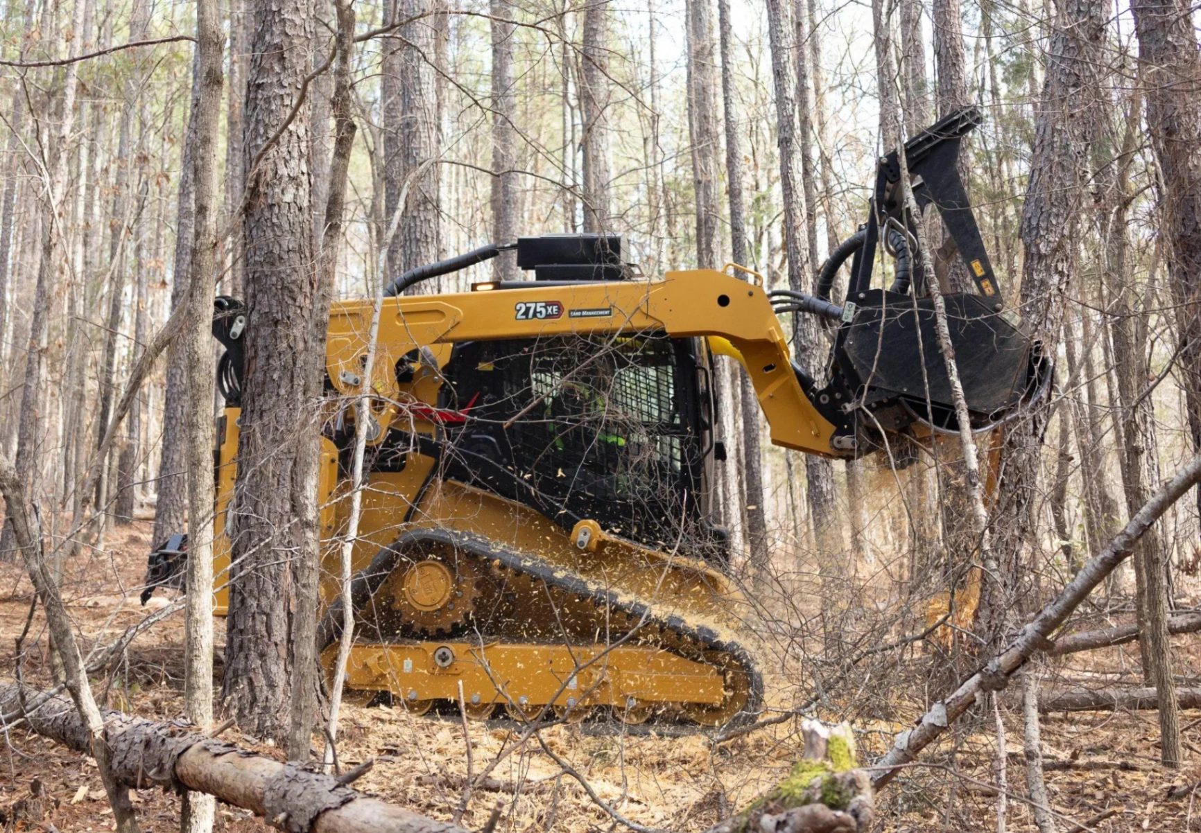 Cat 275 XE compact track loader with forestry mulcher attachment clearing underbrush in a wooded area